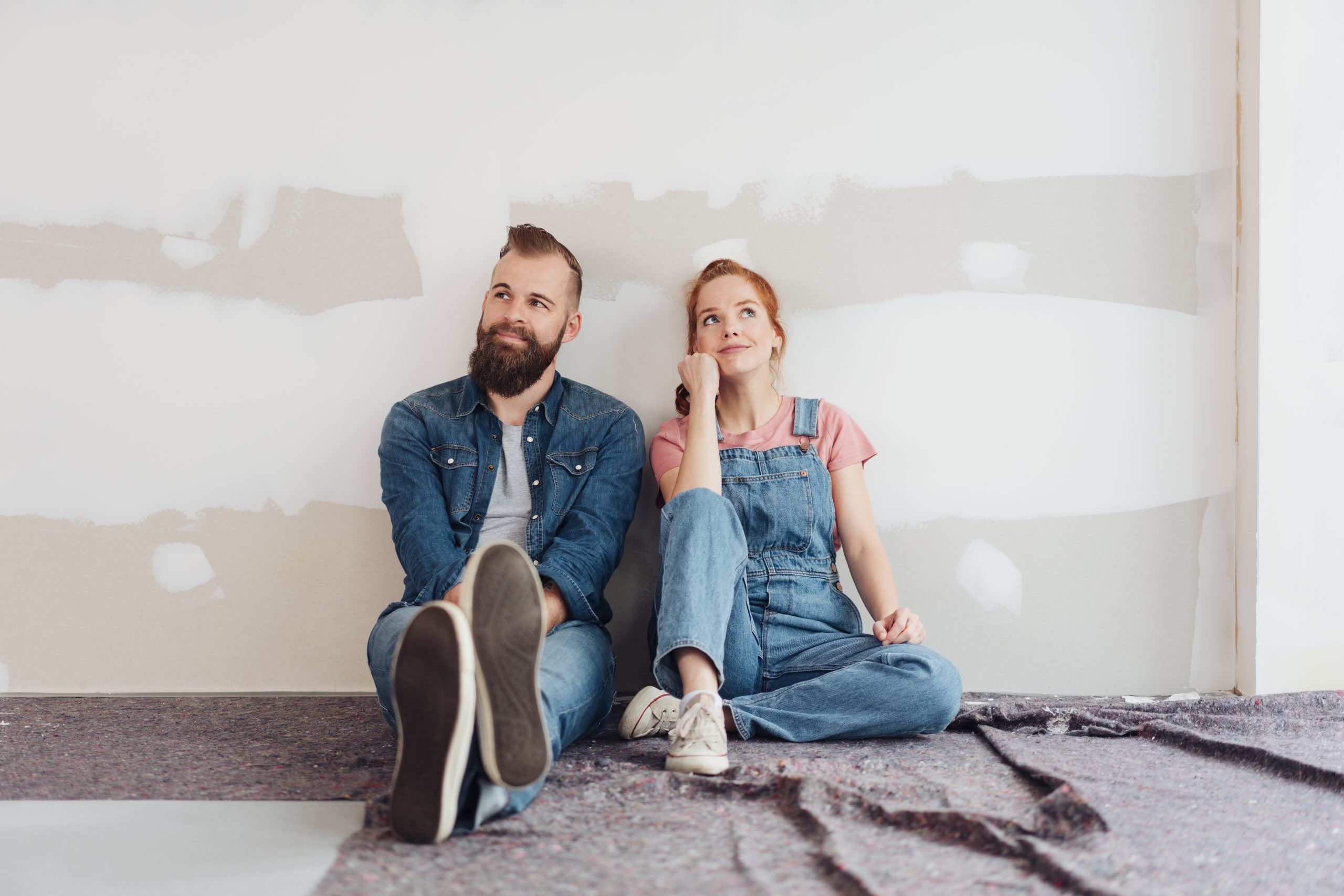 Couple sitting in front of partially painted wall while renovating