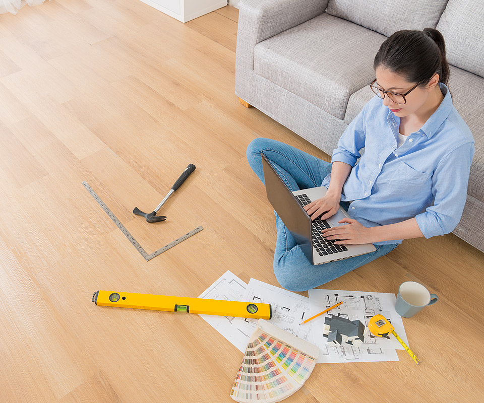 Woman sitting on floor of home with a laptop surrounded by paint samples and construction tools