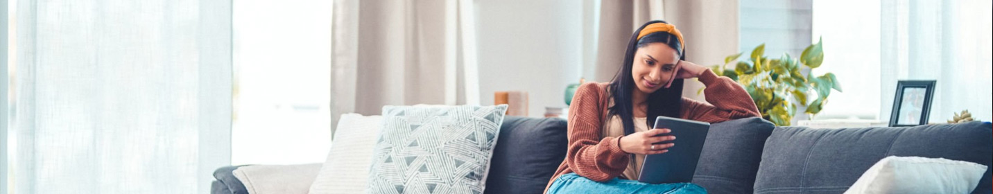 Young woman relaxes on couch while reading on a tablet