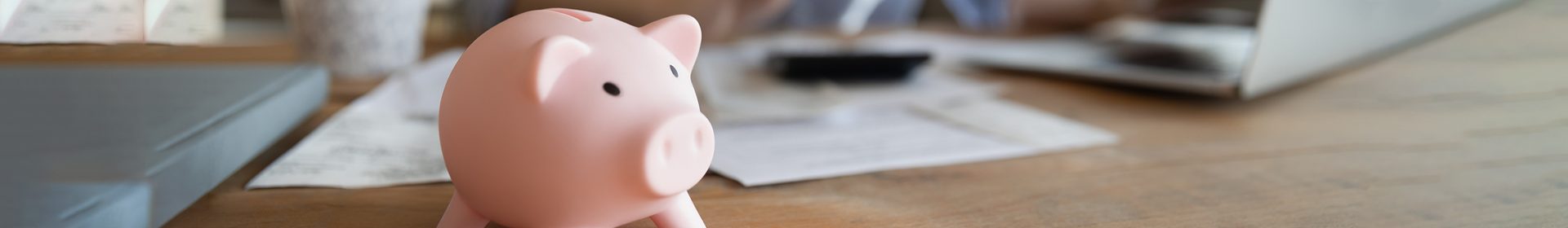 Close up of piggy bank on desk with paperwork and laptop