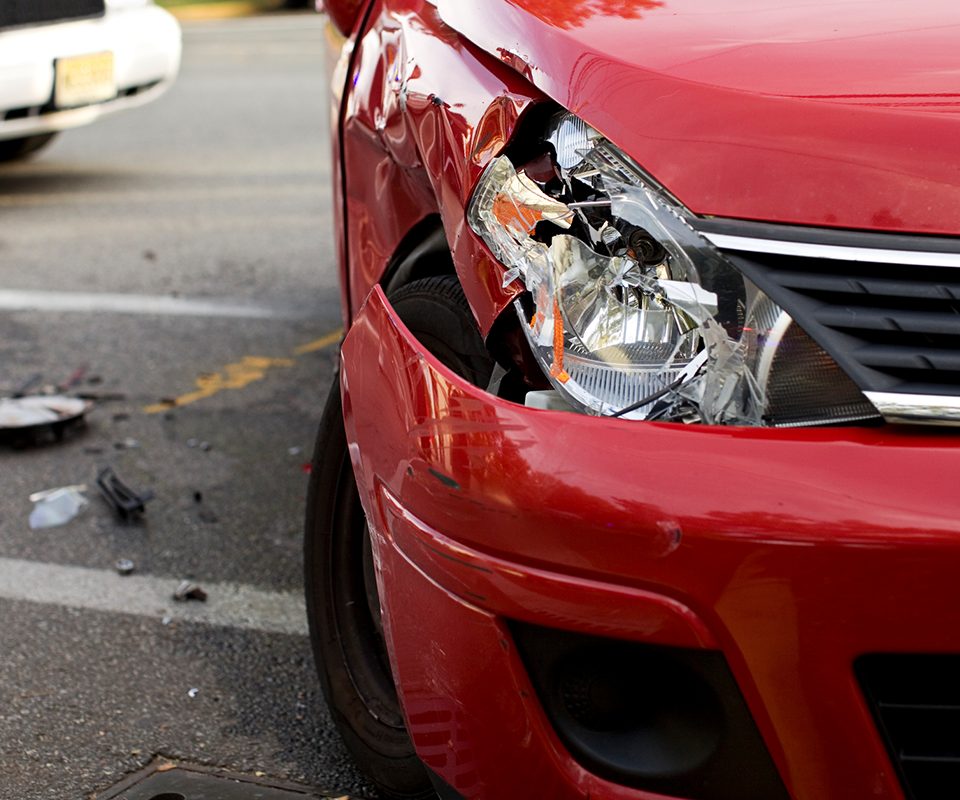 Close up of damaged front of car after car accident; debris scattered nearby