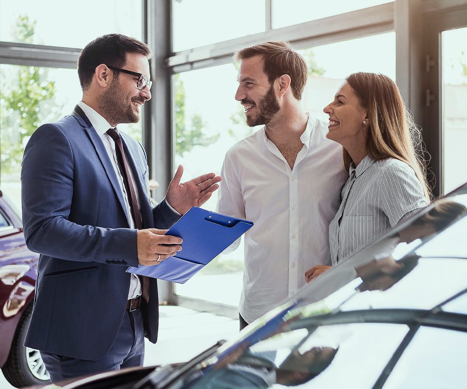 Smiling couple talking to auto salesman next to vehicle