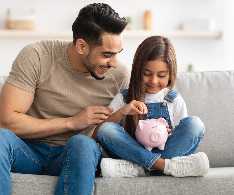 Father and young daughter adding coins to a piggy bank