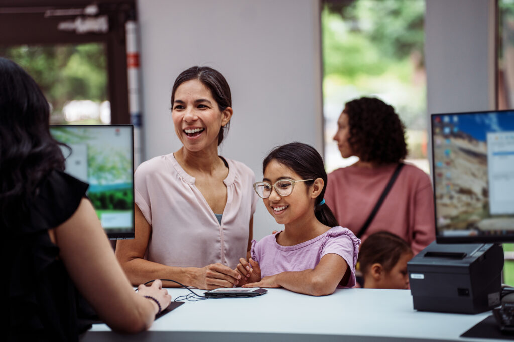 A preteen girl of Latin American descent and her mother smile with excitement while opening a savings account at a credit union.