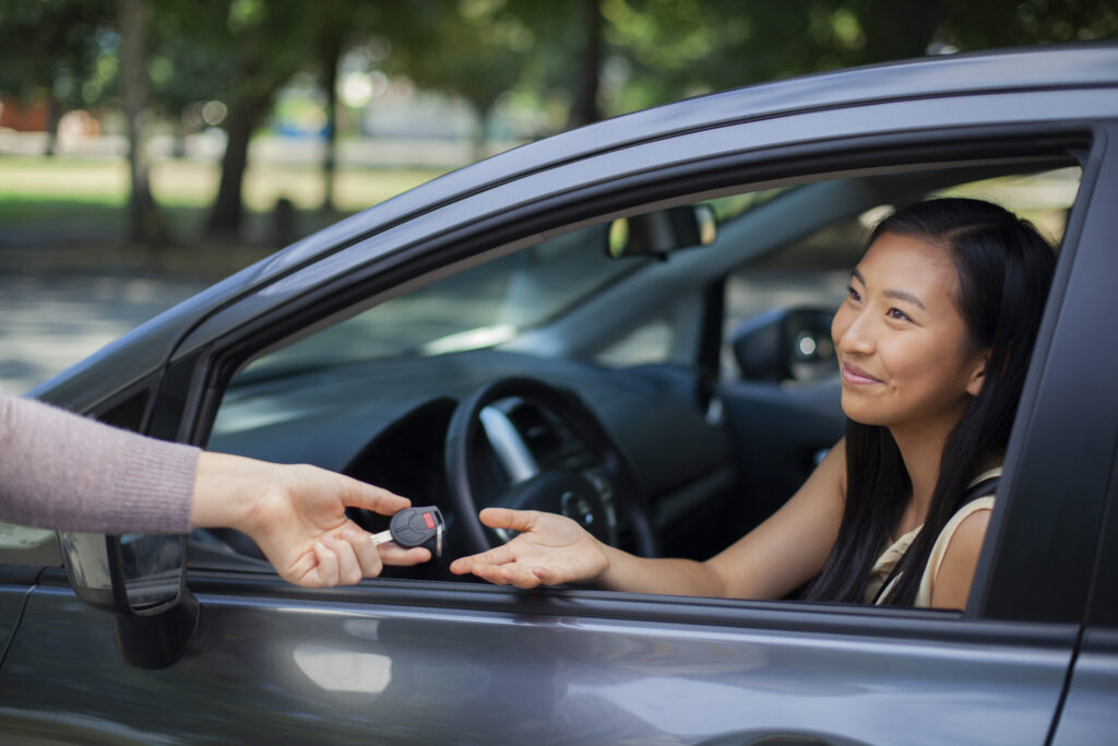 Young Asian Chinese teenage girl new driver receives car key to vehicle car rental buying car borrowing car