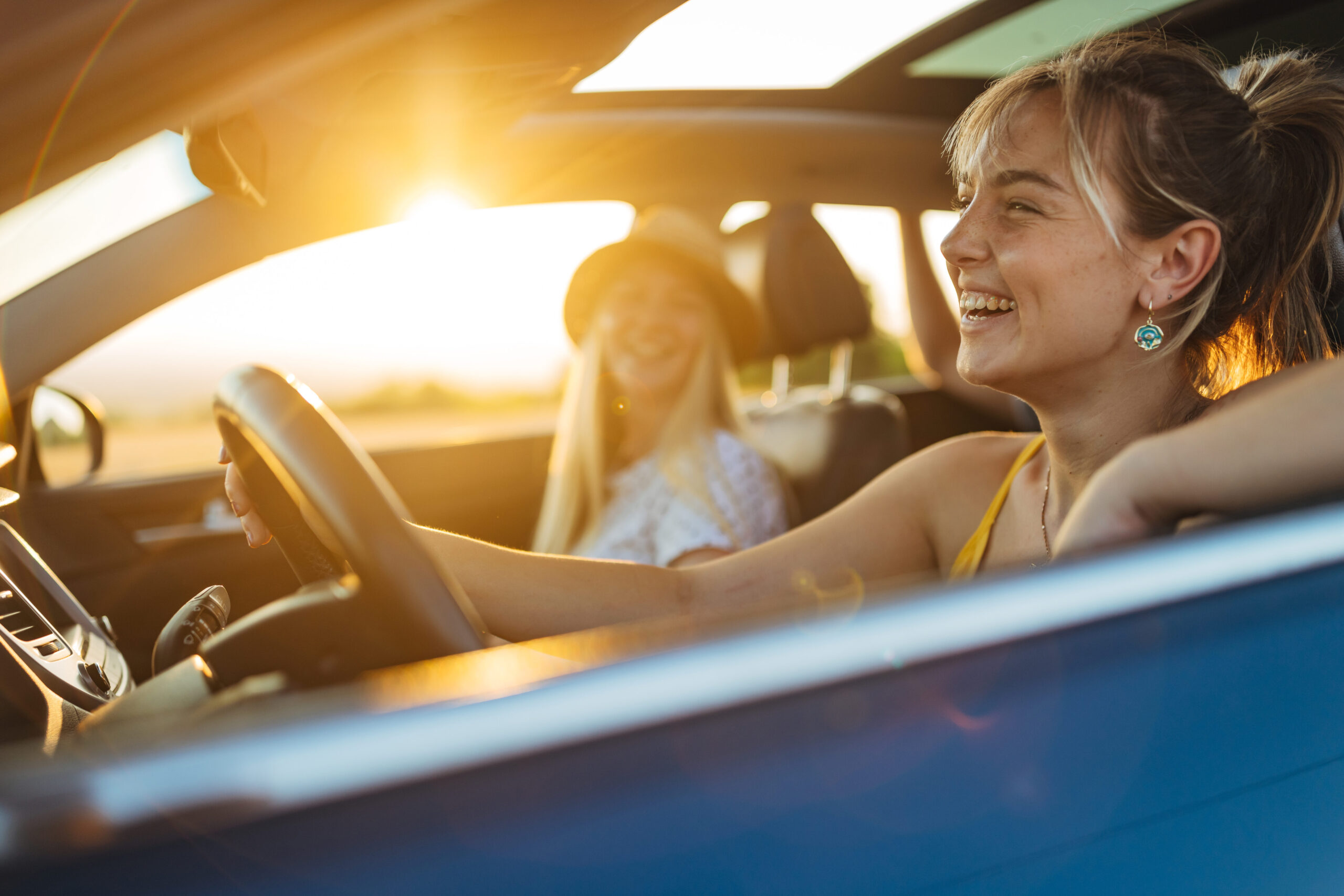 two Gen Z girls enjoying a ride in their new car with the windows down and the sunroof open