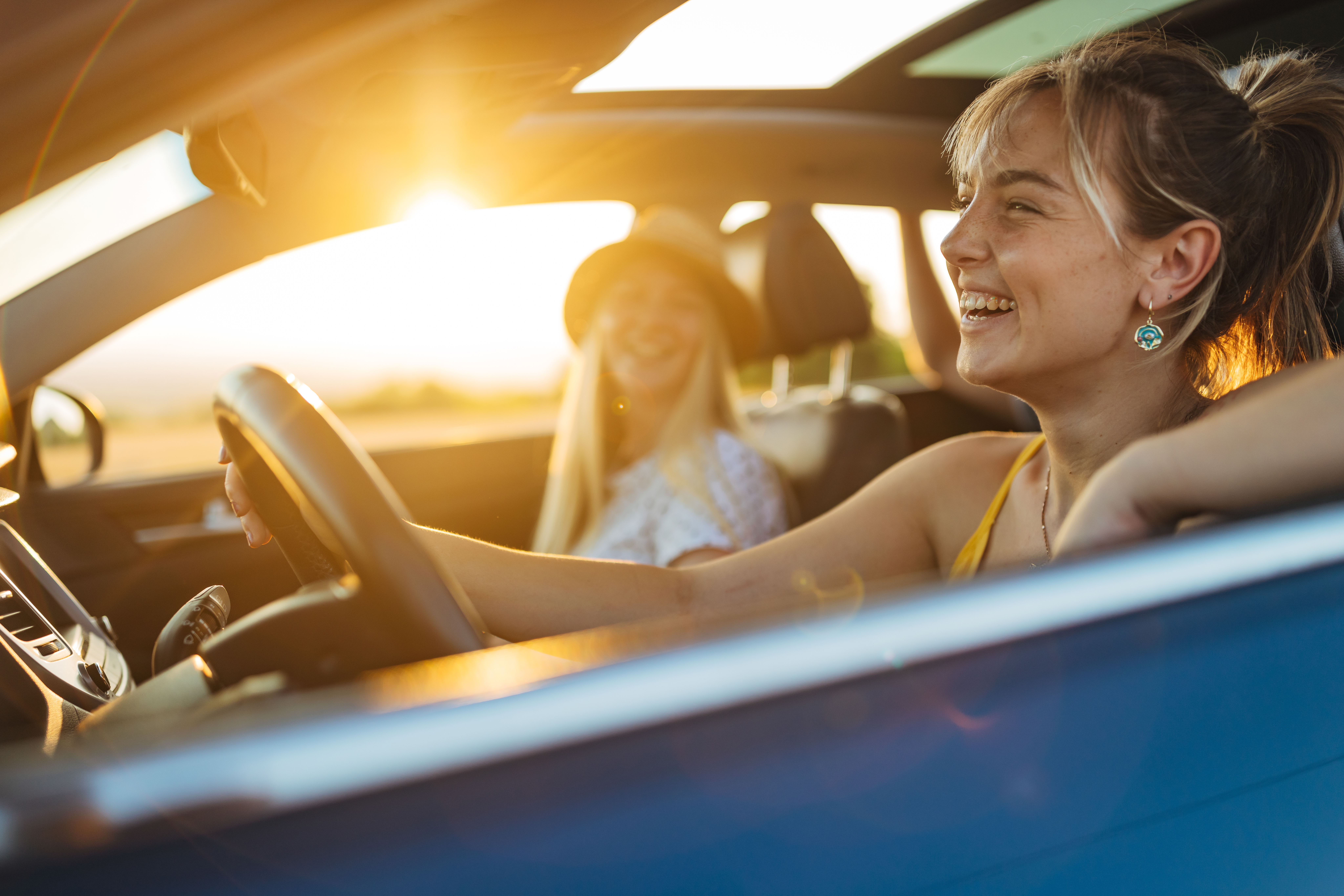 two Gen Z girls enjoying a ride in their new car with the windows down and the sunroof open